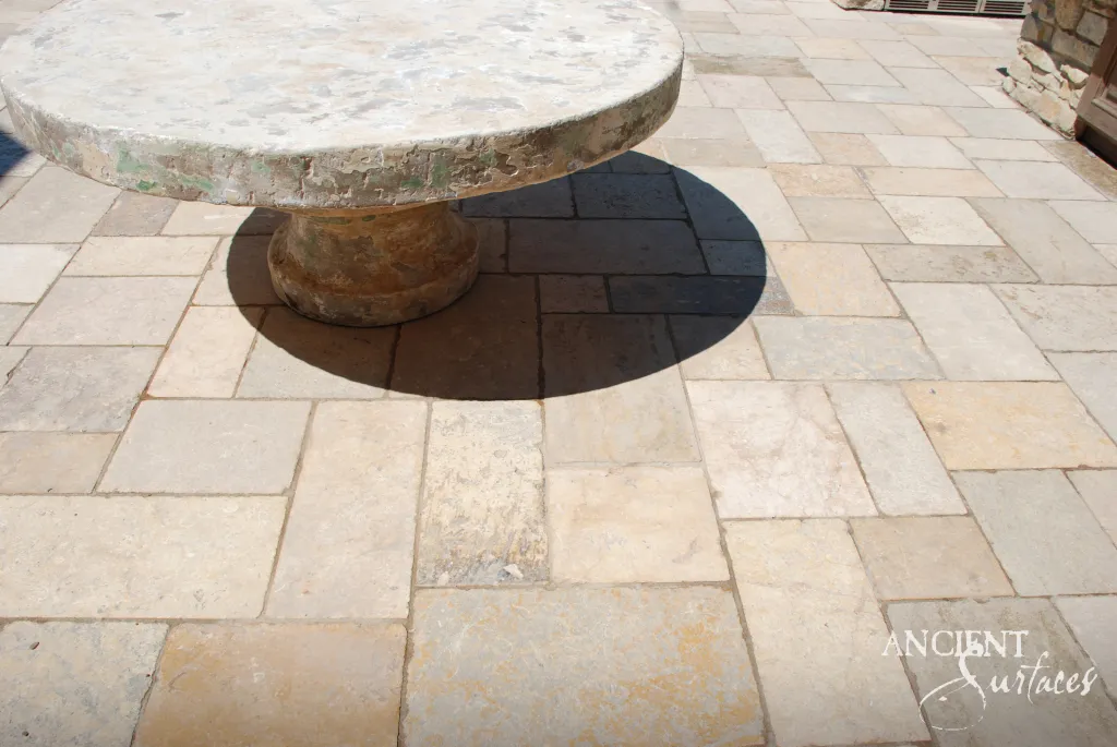 Round antique limestone table with a weathered top and turned pedestal base standing on reclaimed French limestone terrace paving