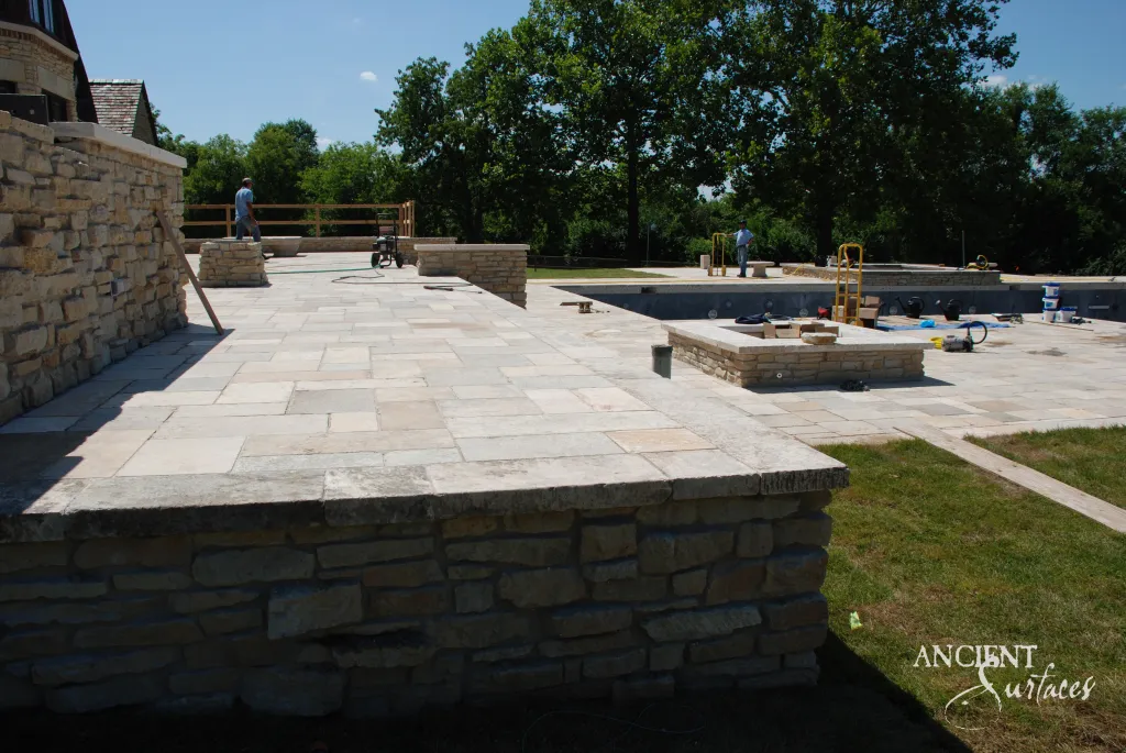 Reclaimed French limestone terrace slabs running above a coursed stone wall capped in antique limestone coping