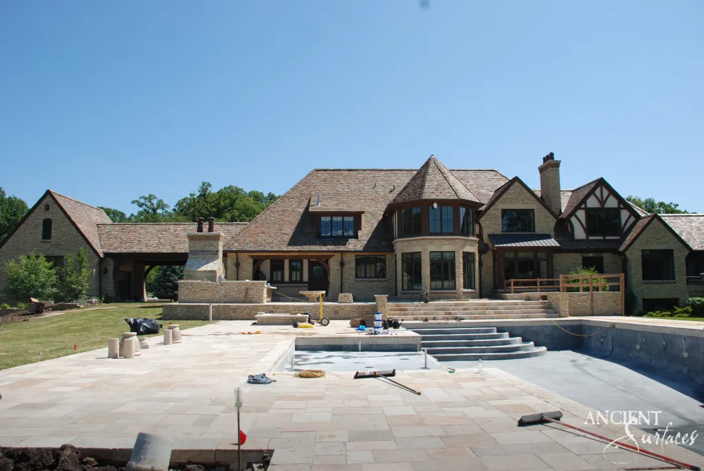 Antique limestone pool coping and terrace paving being set around a new swimming pool behind a gabled stone house
