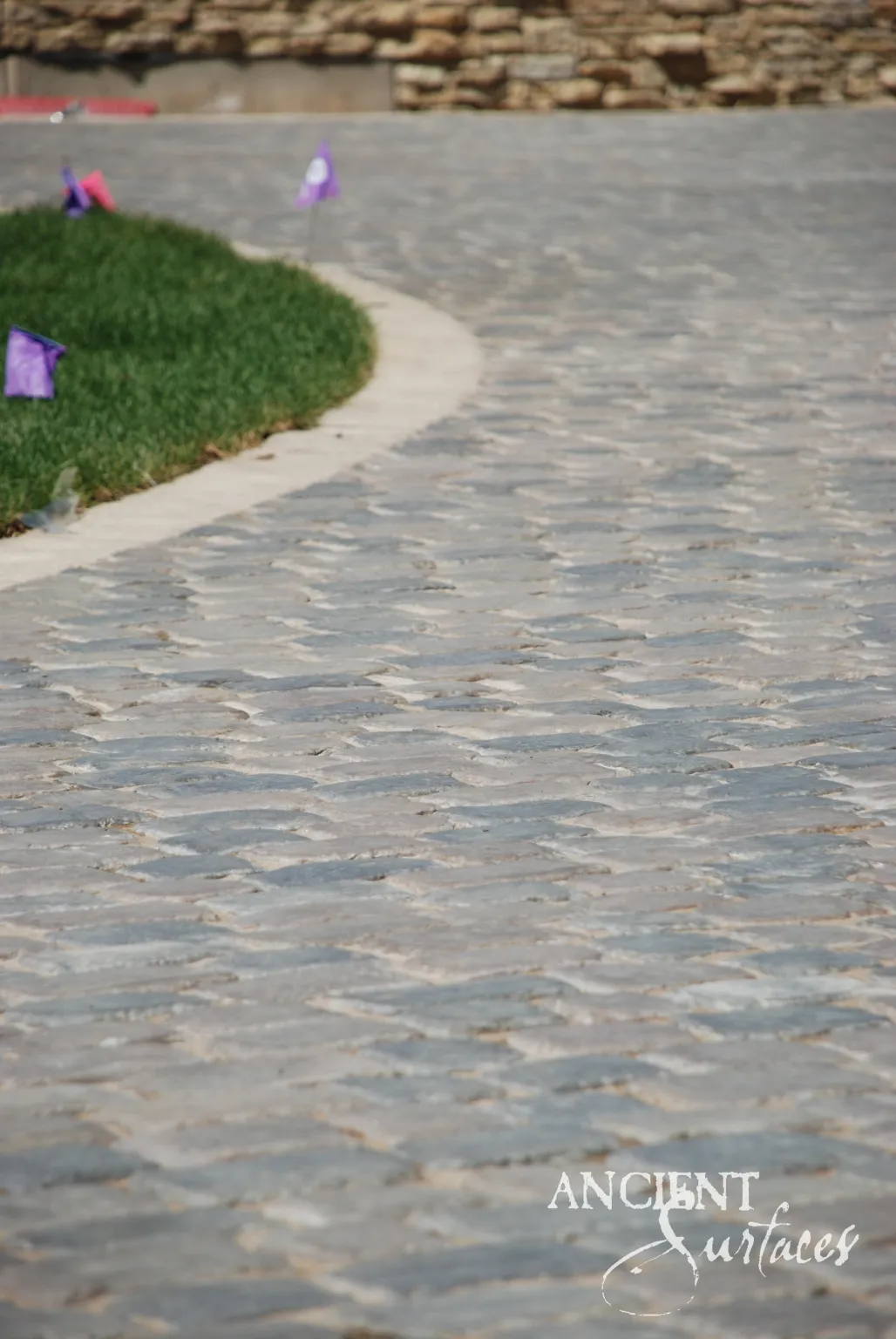 Reclaimed limestone cobblestone paving curving around a lawn edge below a dry stacked stone retaining wall