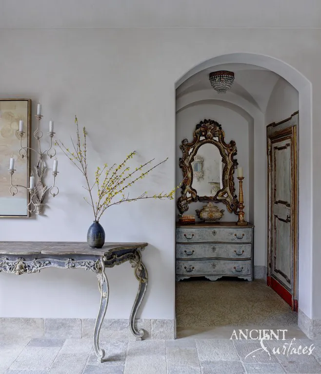 Reclaimed limestone floor pavers in soft worn shades running through an arched entry hall past a carved console table