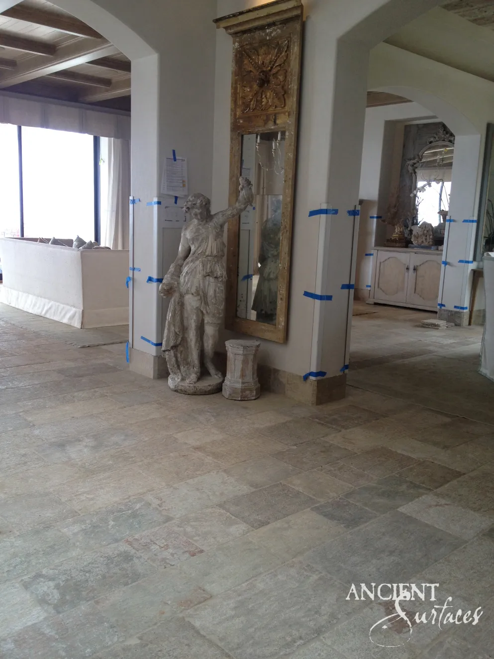 Salvaged stone statue and carved stone plinth standing on antique limestone flooring between plastered archways