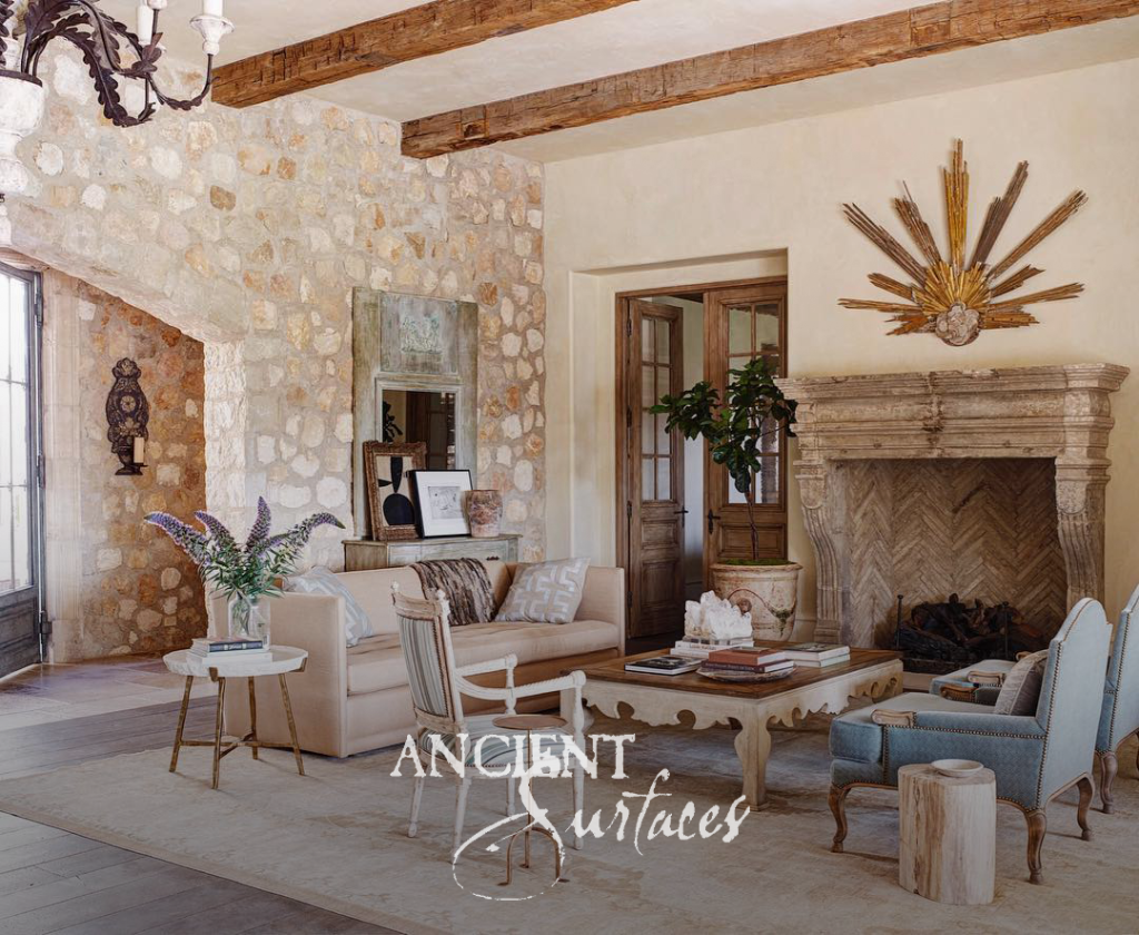 Carved limestone fireplace mantel with a herringbone firebox against a rough limestone masonry wall under exposed timber beams
