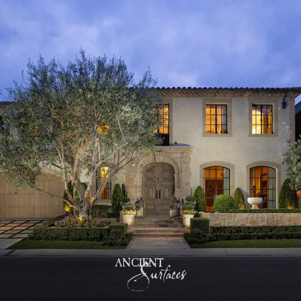 Mediterranean residence at dusk with a carved limestone entry surround, limestone entry steps and a low coursed stone garden wall beneath an olive tree