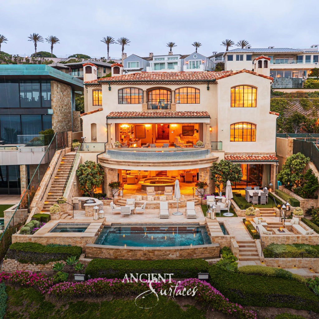 Terraced coastal estate with reclaimed limestone cladding, stone pool surrounds and stone stairways descending to a lit swimming pool at dusk