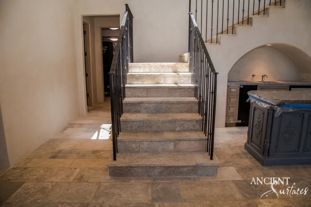 Millennium limestone staircase with thick stone treads rising from antique Barr limestone floor pavers beside a wrought iron rail