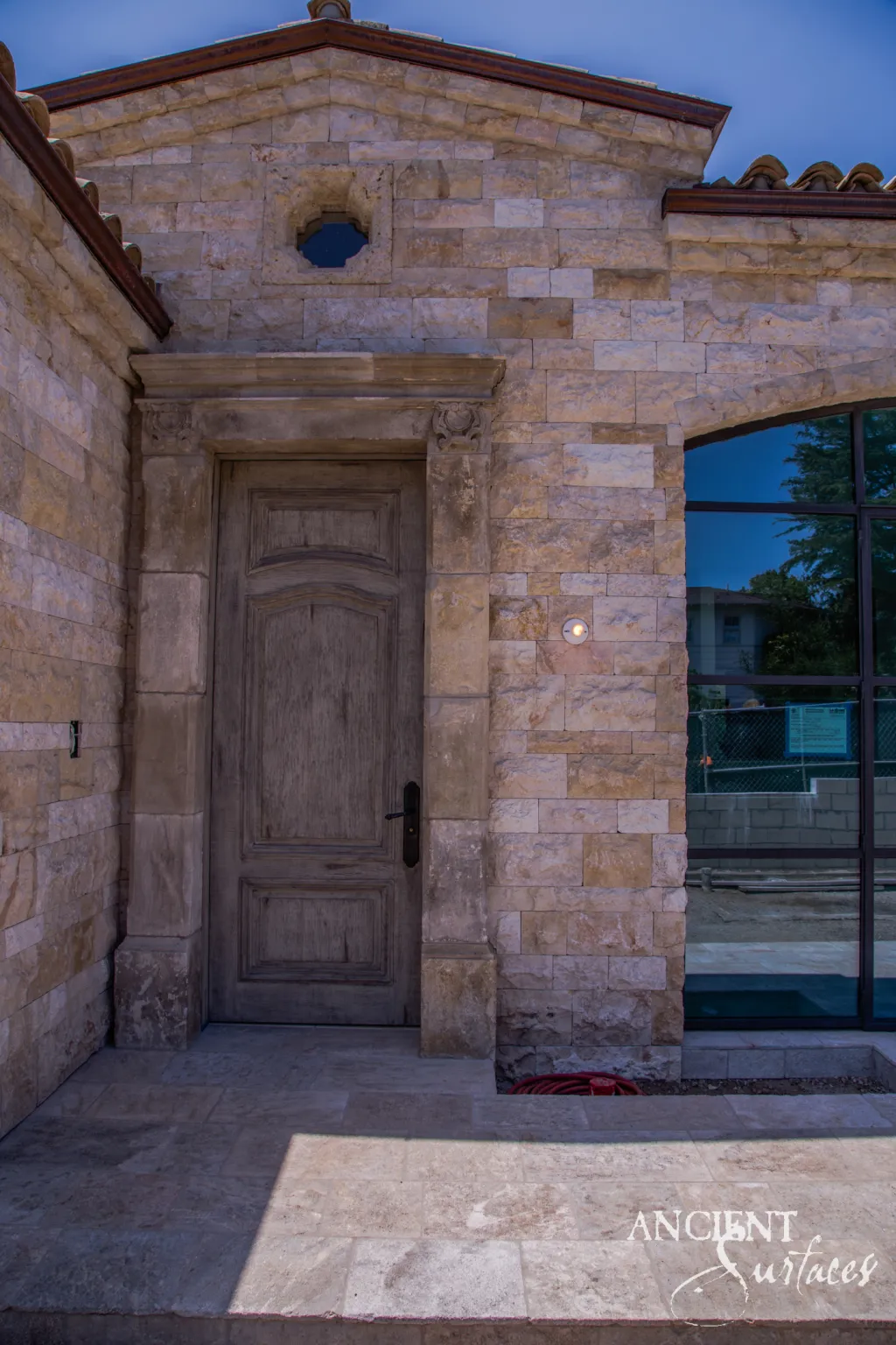 Golden biblical stone wall cladding framing a carved limestone door surround and an antique wooden entry door at dusk