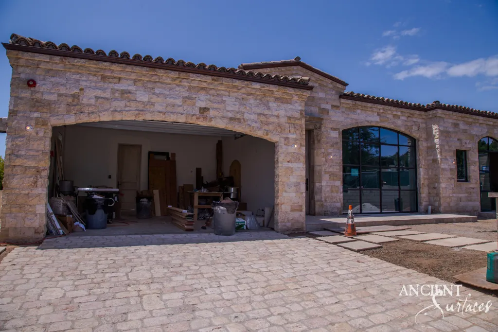 Villa facade clad in biblical stone above a reclaimed antique cobblestone limestone driveway under a tiled roofline